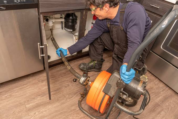Plumber using a drain snake machine to clear a recurring clog in San Jacinto, CA