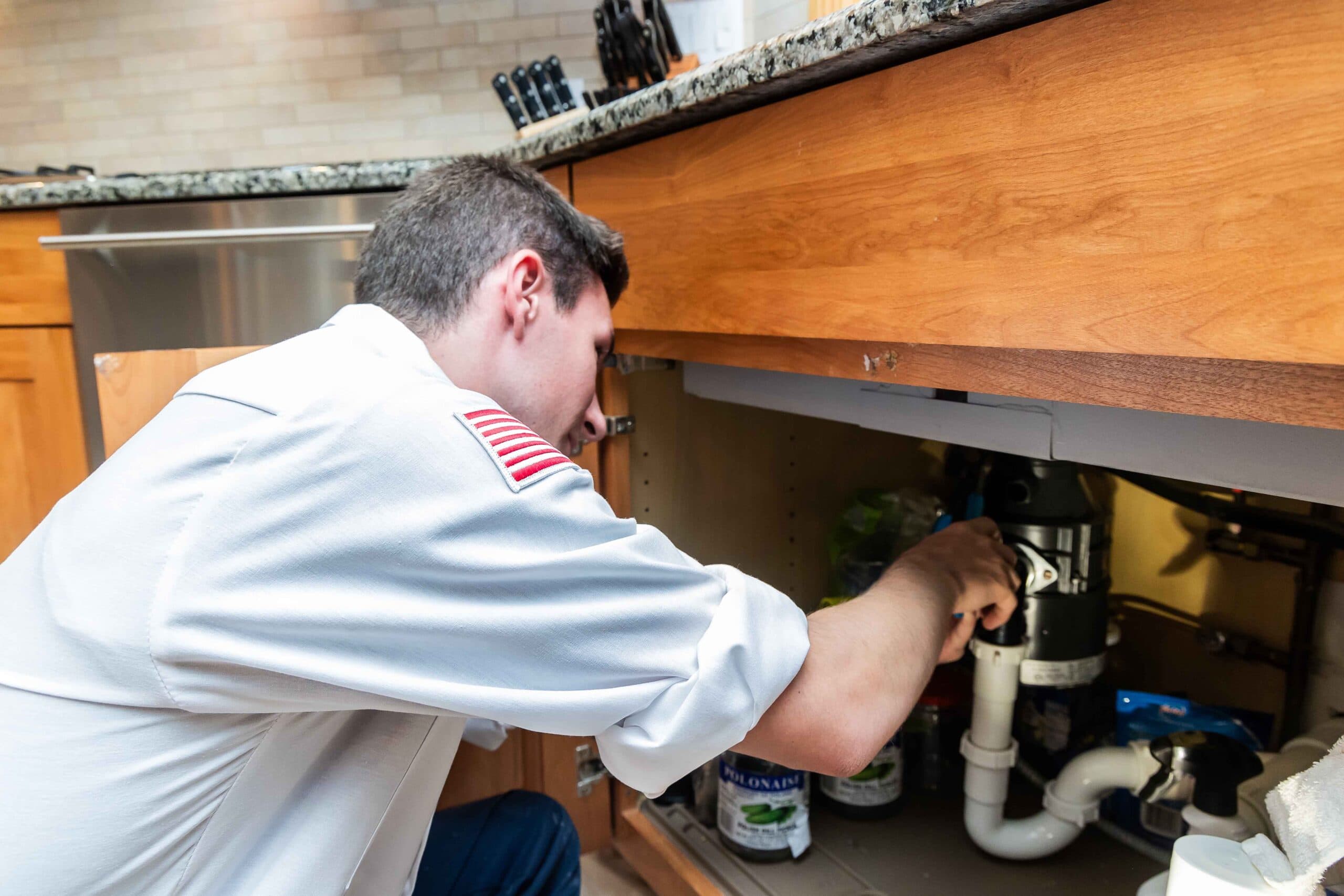 America's Plumbing technician servicing a garbage disposal under a kitchen sink in San Jacinto, CA
