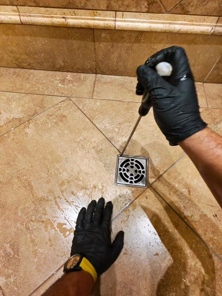 Plumber manually clearing a shower floor drain instead of using chemical cleaner in San Jacinto, CA
